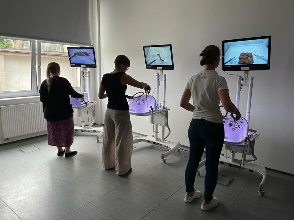 na sali szkoleniowej stoją 3 osoby odwrócone tyłem przed symulatorami medycznymi wykonując procedurę chirurgiczną uwidocznioną na ekranach monitorów