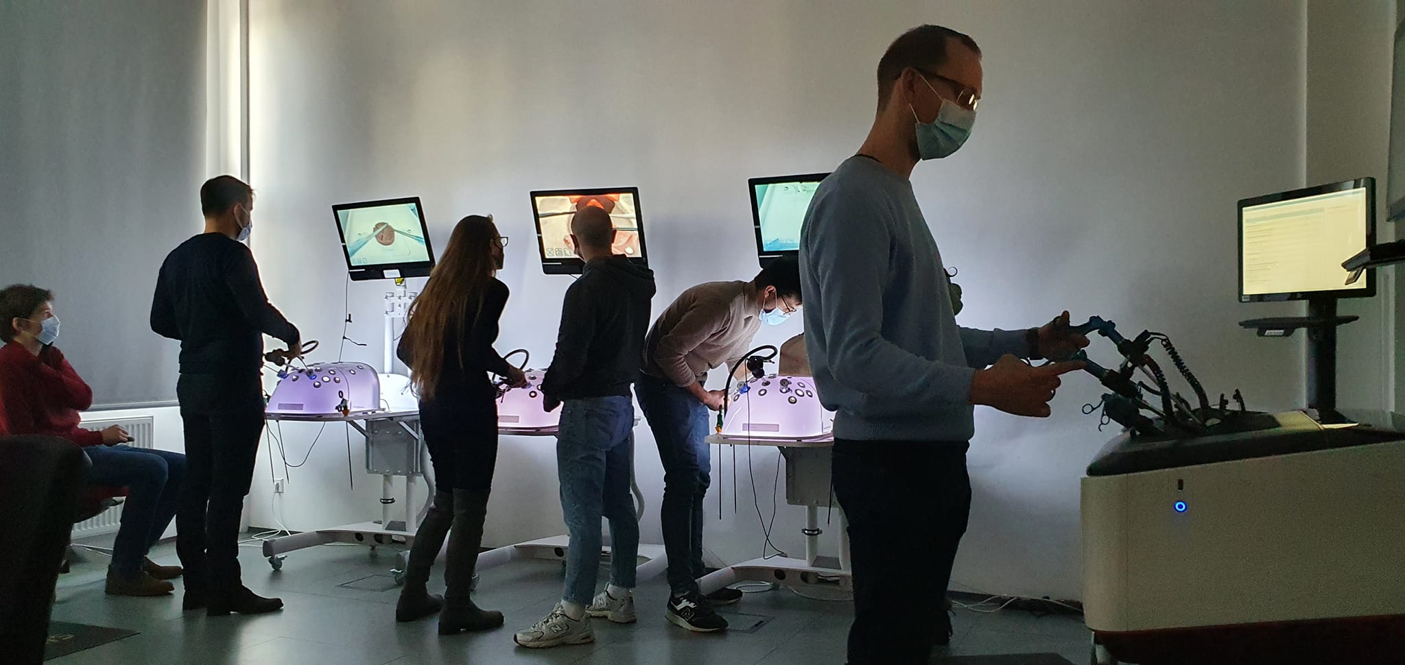 na sali szkoleniowej znajduje się 6 osób odwróconych bokiem oraz tyłem przed symulatorami medycznymi wykonując procedurę chirurgiczną uwidocznioną na ekranach monitorów